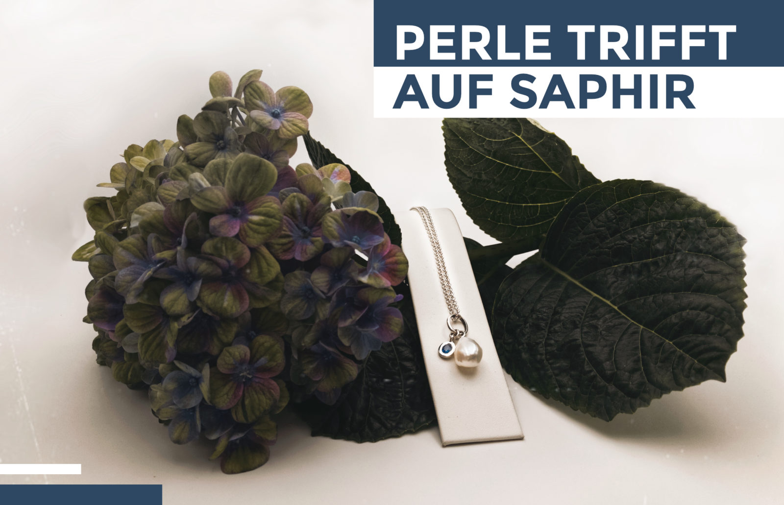 Neuigkeiten: "Perle trifft auf Saphir" - Kette mit Perle und eingefasstem Saphir auf Hortensienblüte dekoriert